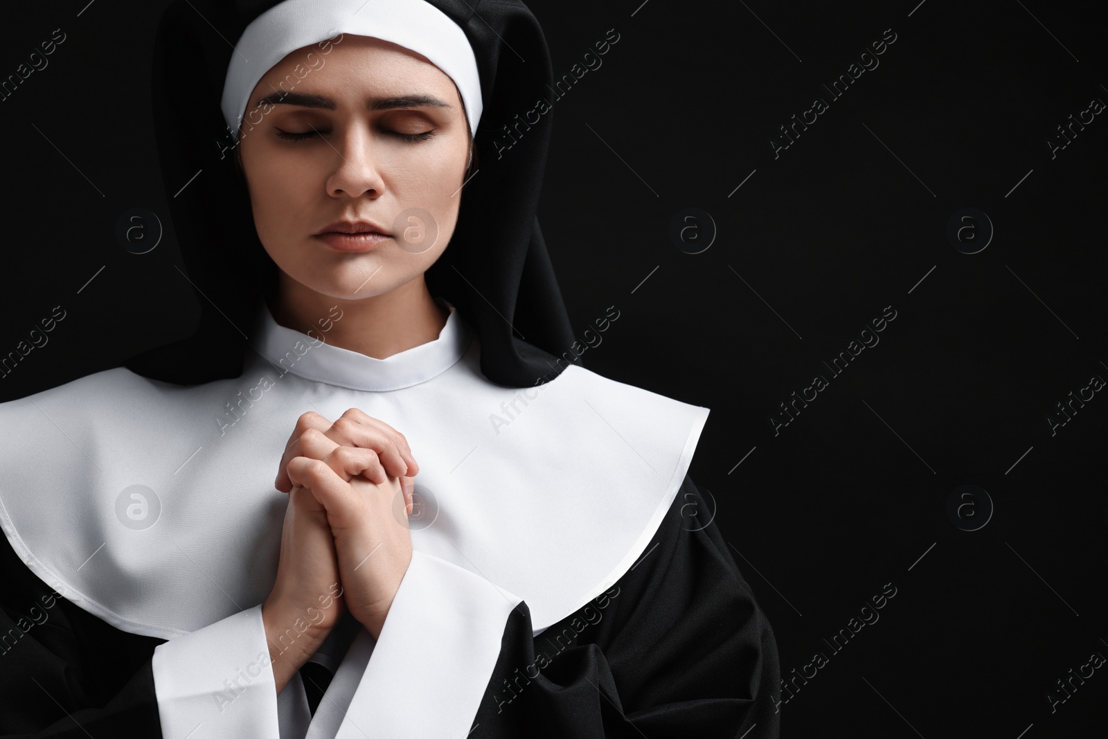 Photo of Nun with clasped hands praying to God on black background. Space for text