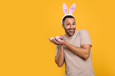 Happy African American man in bunny ears headband with Easter eggs on orange background, space for text
