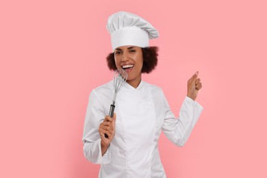Photo of Happy female chef with whisk singing on pink background