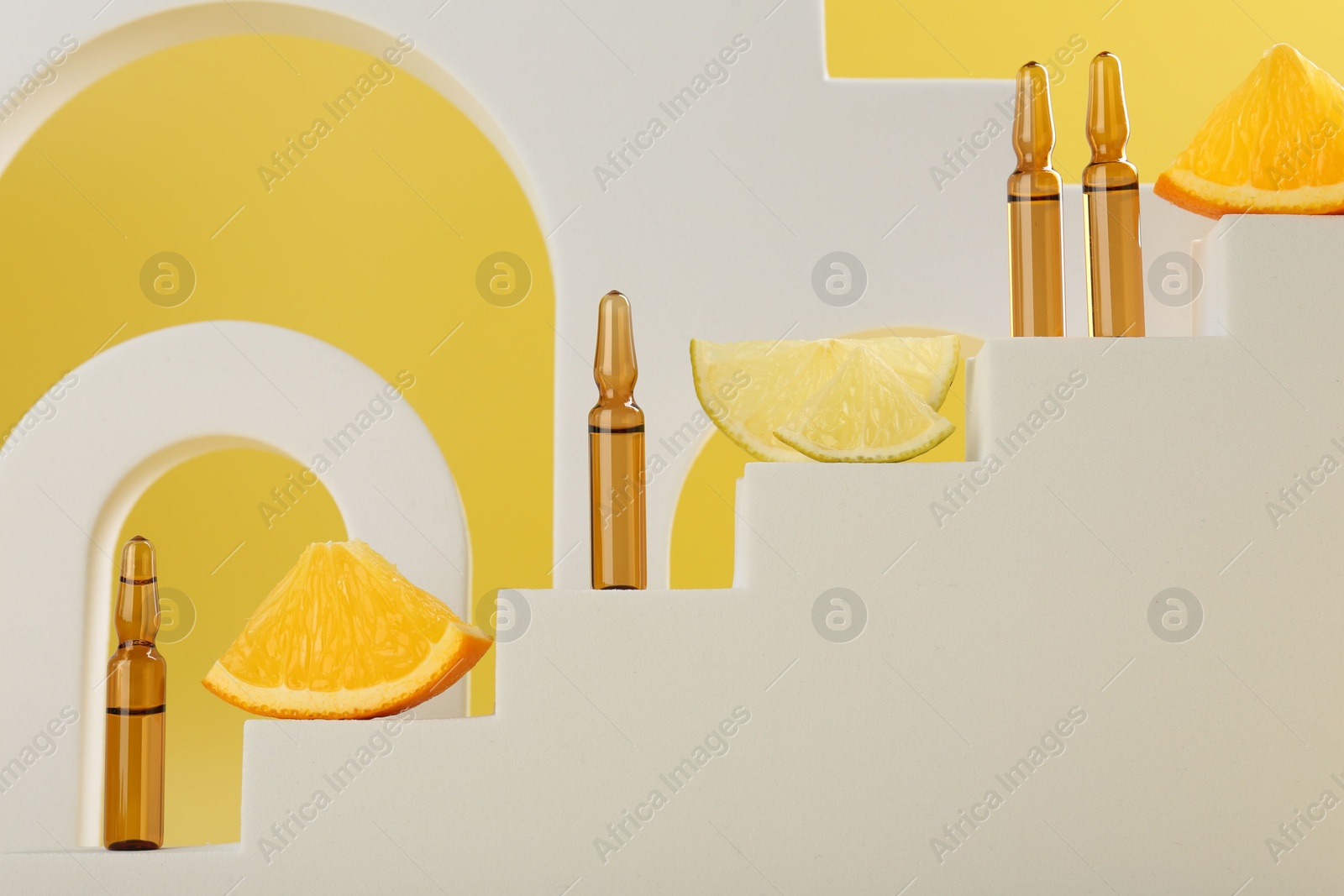 Photo of Stylish presentation of skincare ampoules with vitamin C and citrus slices on decorative stairs against yellow background, closeup