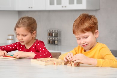 Photo of Happy children playing with different math game kits at white marble table in kitchen. Study mathematics with pleasure