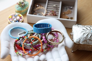 Photo of Ceramic hand stand with many stylish bracelets and jewelry boxes on wooden table, closeup