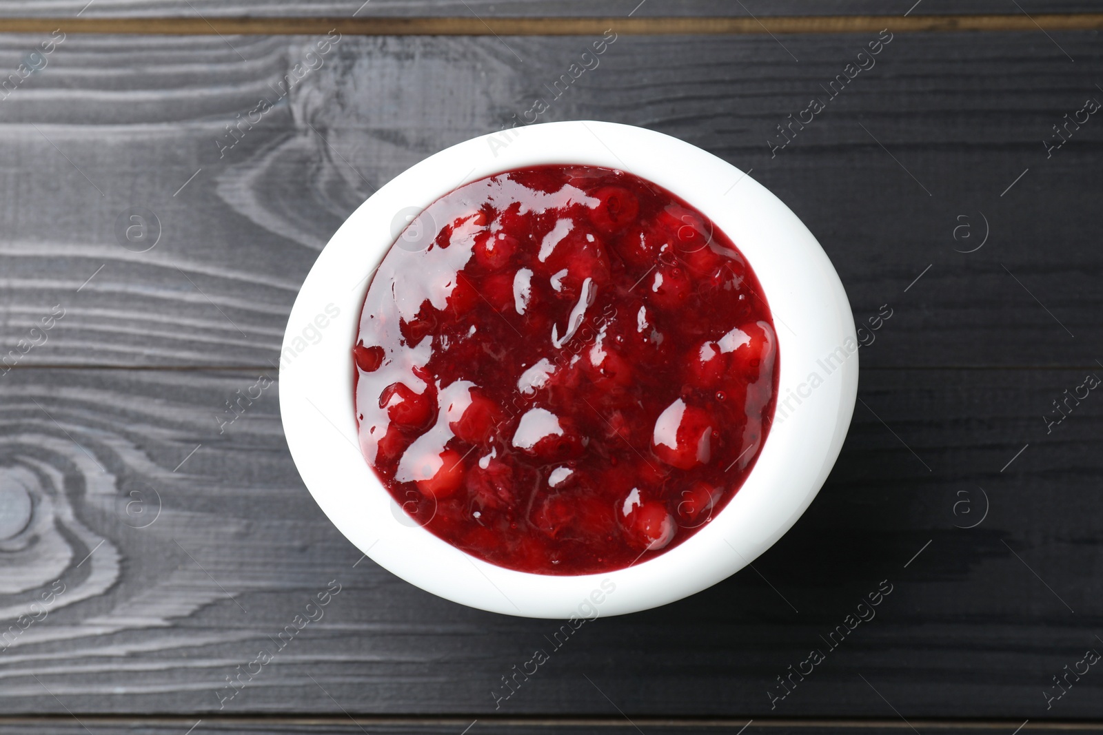 Photo of Fresh cranberry sauce in bowl on black wooden table, top view