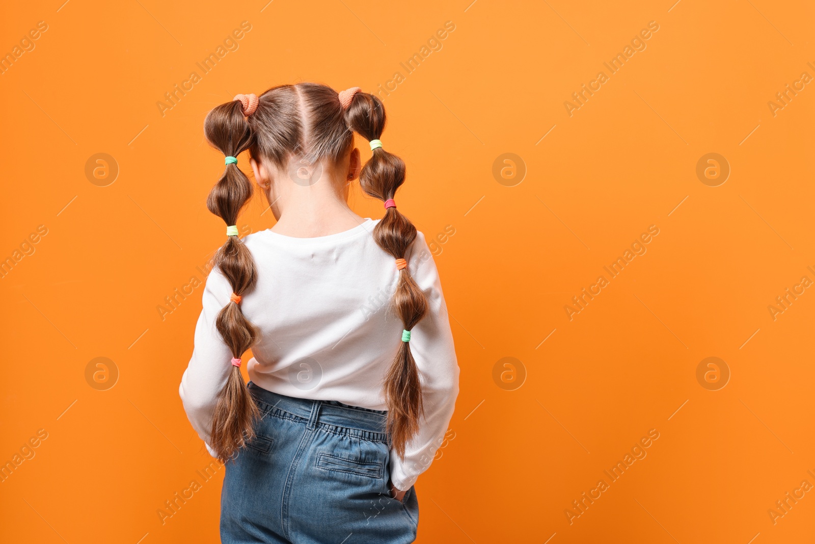Photo of Little girl with beautiful hairstyle on orange background, back view. Space for text
