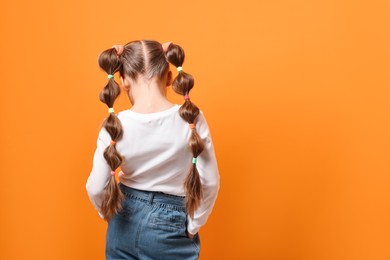 Little girl with beautiful hairstyle on orange background, back view. Space for text