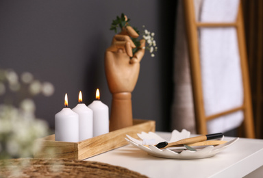 Photo of White table with burning candles and toothbrushes in bathroom