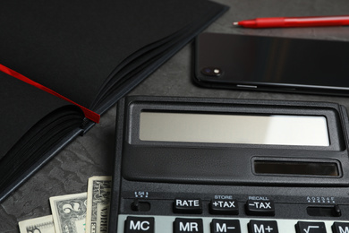 Photo of Calculator, money, smartphone and notebook on dark grey table, closeup. Tax accounting