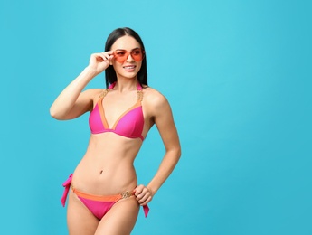 Photo of Beautiful young woman in stylish bikini with sunglasses on light blue background. Space for text