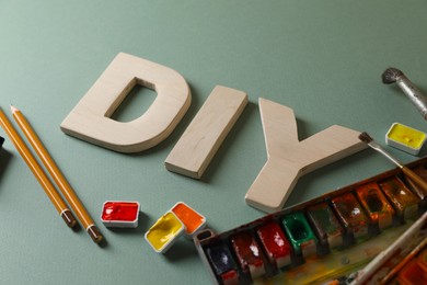 Photo of Abbreviation DIY made of letters and different painting supplies on pale green background, closeup