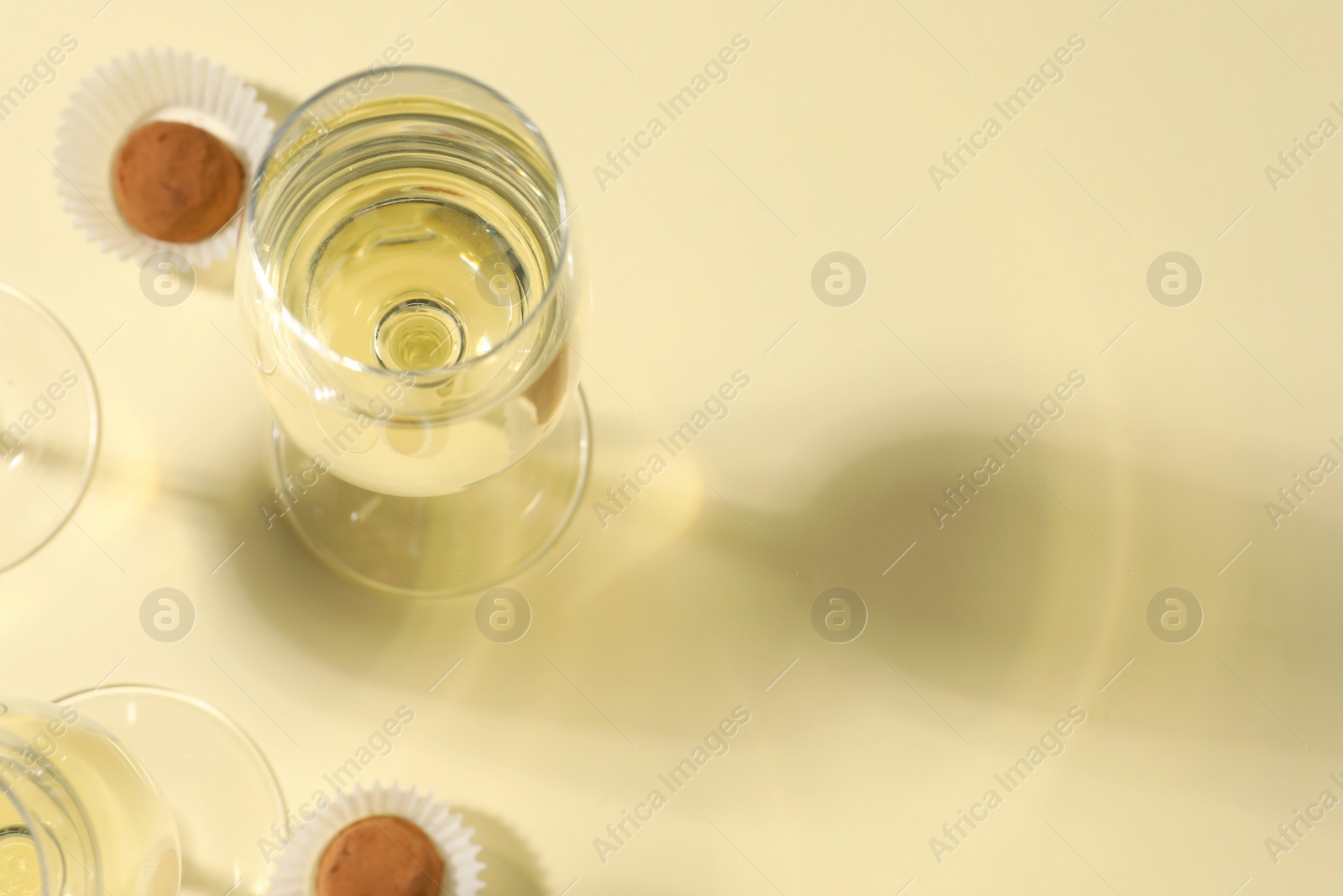 Photo of Glasses of delicious sparkling wine and chocolate truffles on light yellow background, above view. Space for text