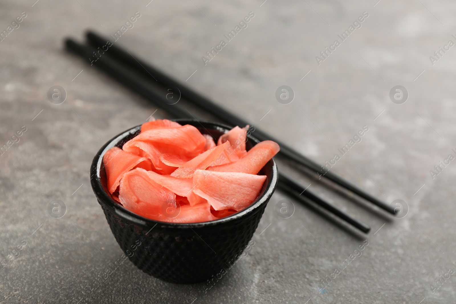 Photo of Pickled ginger in bowl and chopsticks on light grey table, space for text