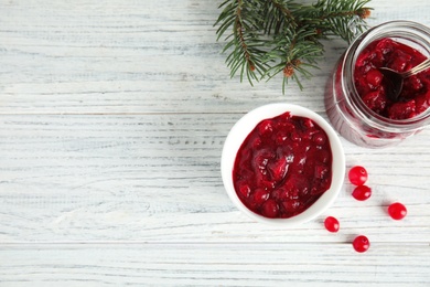 Photo of Bowl and jar with tasty cranberry sauce on white wooden background, flat lay. Space for text