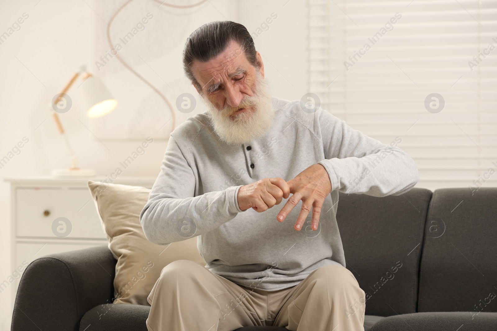 Photo of Senior man suffering from pain in hand on sofa at home. Rheumatism symptom