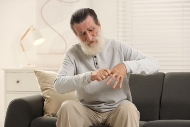 Photo of Senior man suffering from pain in hand on sofa at home. Rheumatism symptom