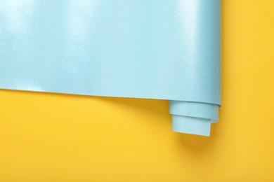 Roll of turquoise wrapping paper on yellow background, top view