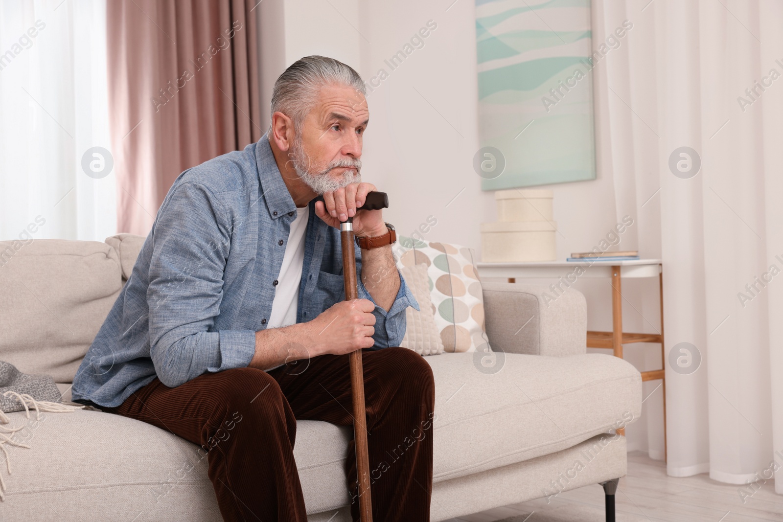 Photo of Senior man with walking cane sitting on sofa at home. Space for text