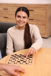 Portrait of beautiful woman playing checkers at coffee table indoors