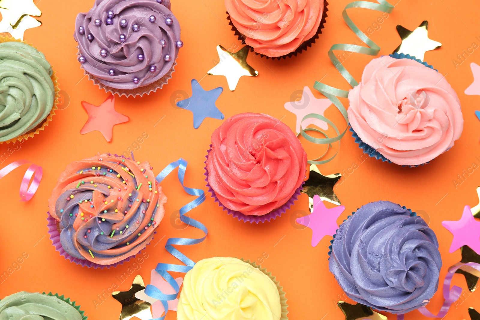 Photo of Delicious cupcakes with bright cream and party decor on orange background, flat lay