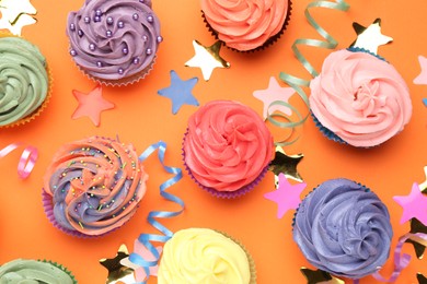 Photo of Delicious cupcakes with bright cream and party decor on orange background, flat lay