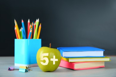 Image of Apple with carved number five and plus symbol as grade. School stationery on white table in classroom, space for text
