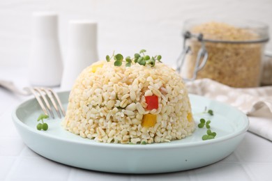 Delicious bulgur with vegetables and microgreens served on table, closeup