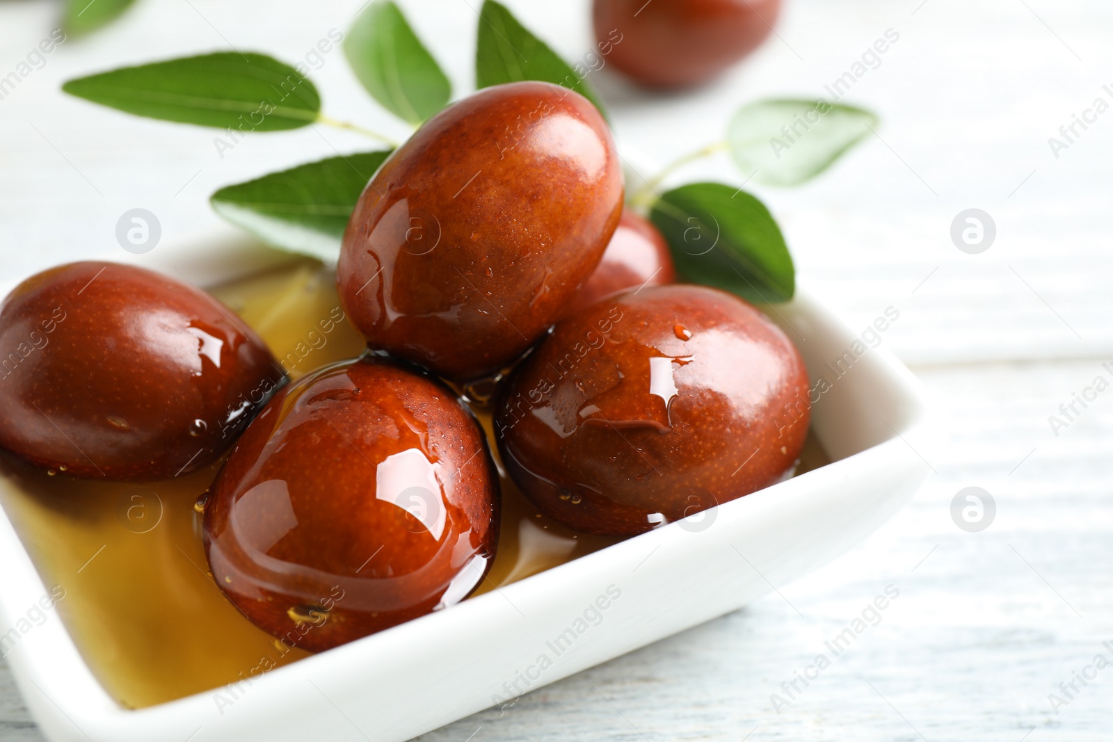 Photo of Sauce boat with jojoba oil and seeds on white wooden table, closeup