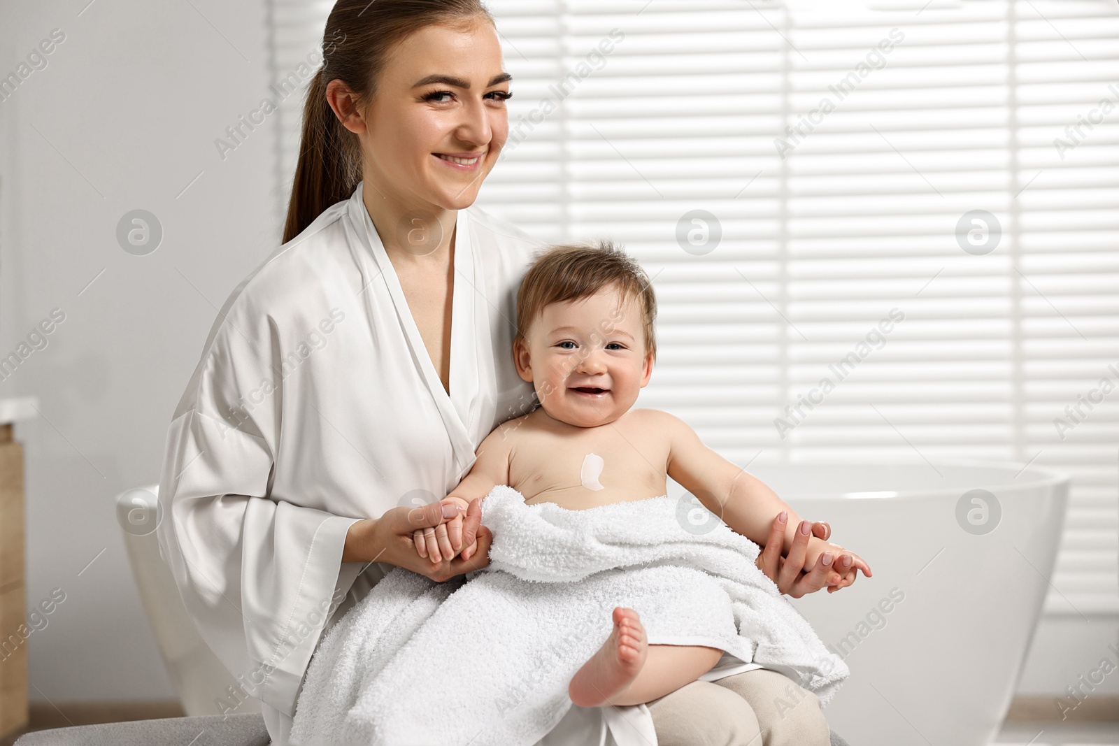 Photo of Happy mother holding her baby with body cream on skin at home