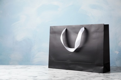 Photo of Paper shopping bag with ribbon handles on table against color background. Mockup for design