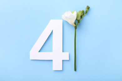 Paper number 4 and beautiful flower on light blue background, top view