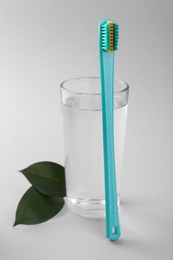 Photo of Plastic toothbrush, glass of water and green leaves on light background