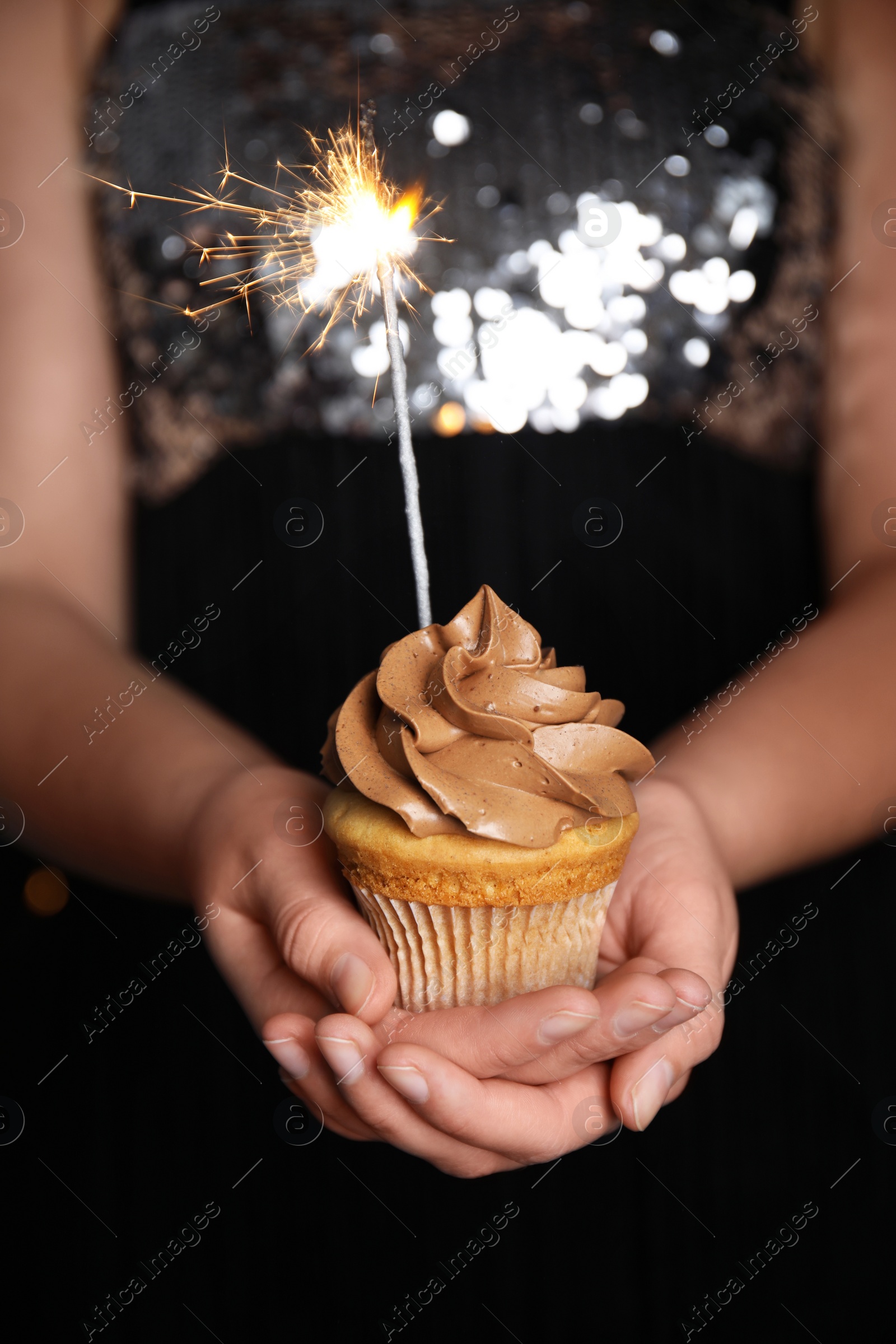 Photo of Woman holding birthday cupcake with sparkler, closeup