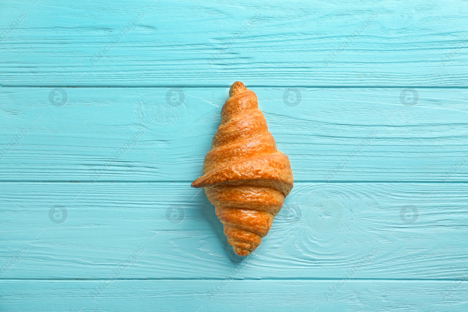 Photo of Tasty croissant on light blue wooden background, top view. French pastry