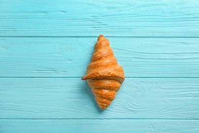 Photo of Tasty croissant on light blue wooden background, top view. French pastry