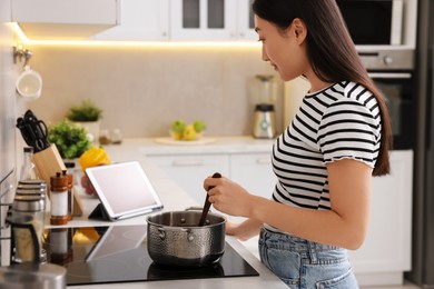 Photo of Woman looking at recipe on tablet while cooking in kitchen