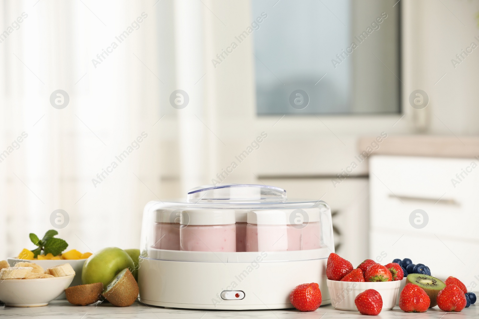 Photo of Modern yogurt maker with full jars and different fruits on white marble table indoors