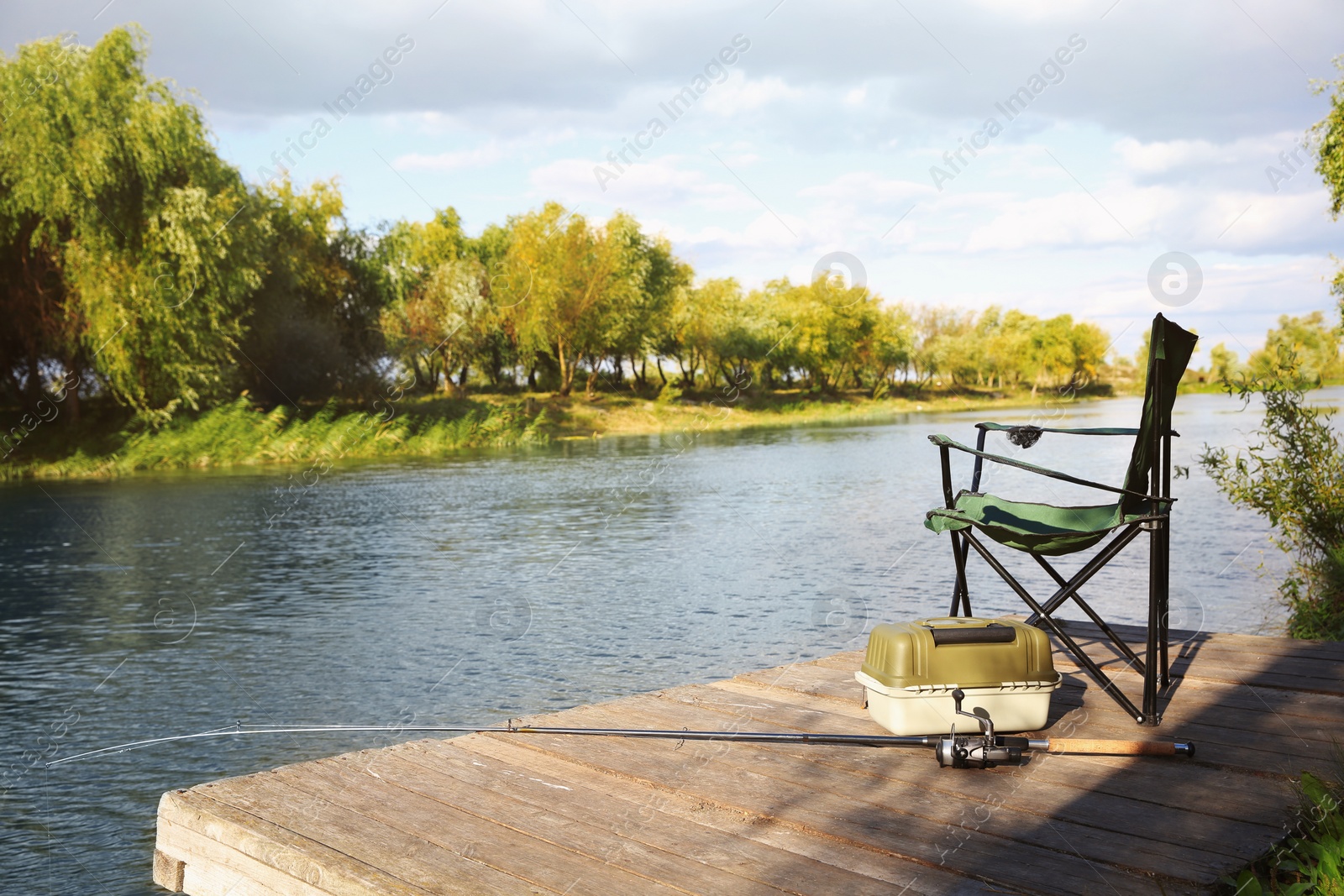 Photo of Folding chair, tackle box and rod for fishing on wooden pier at riverside. Recreational activity