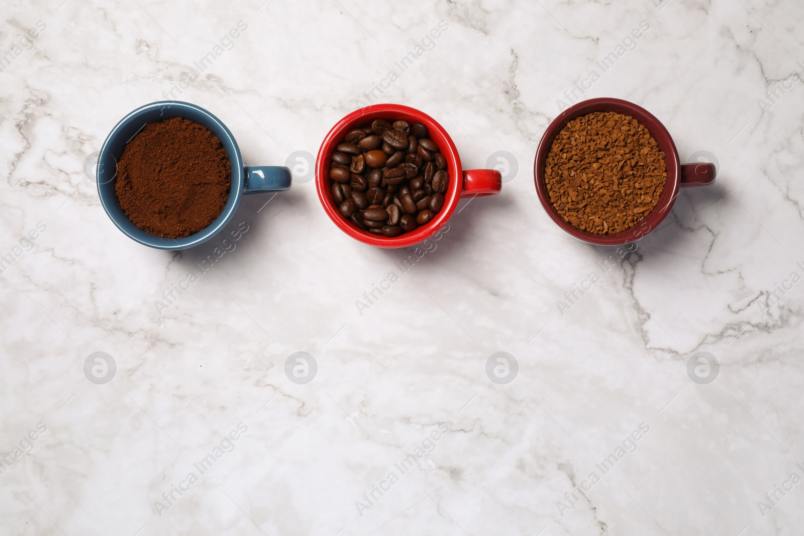 Photo of Instant, ground coffee and roasted beans in cups on white marble table, flat lay. Space for text