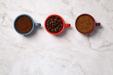 Instant, ground coffee and roasted beans in cups on white marble table, flat lay. Space for text