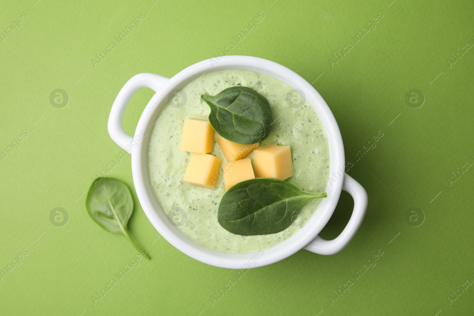 Photo of Delicious spinach cream soup with cheese in bowl on green background, top view