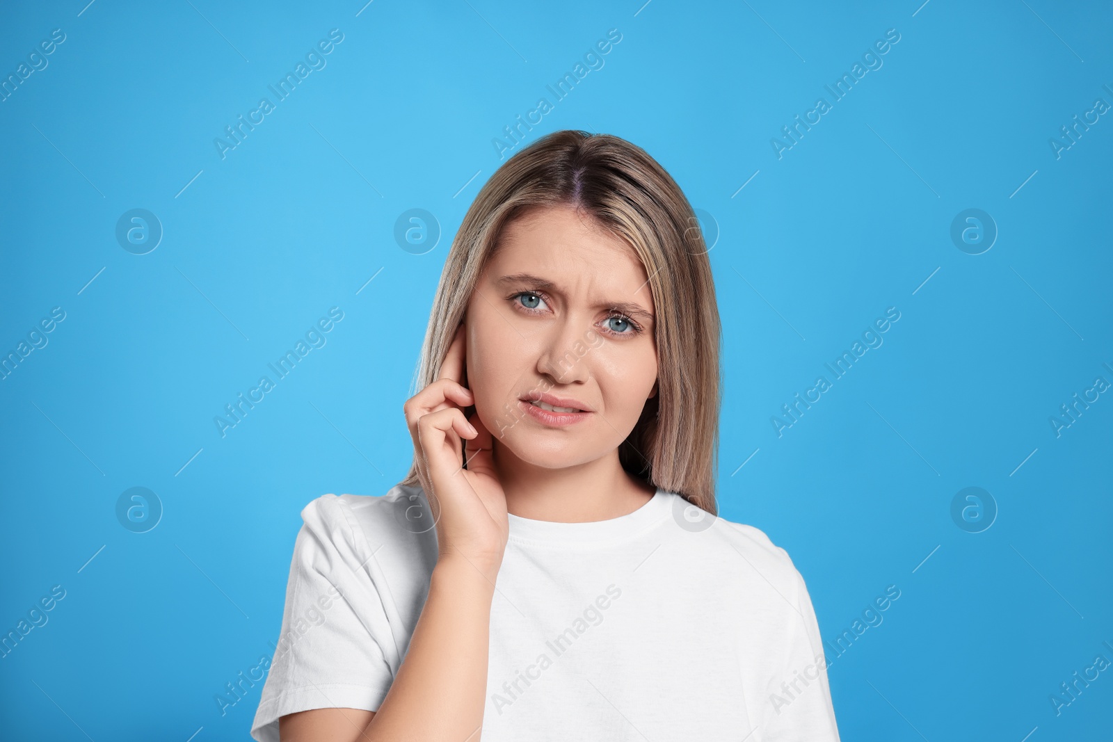 Photo of Young woman suffering from ear pain on light blue background