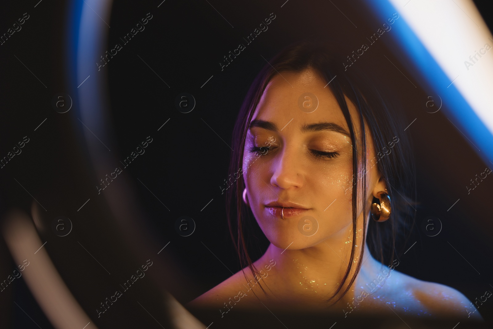 Photo of Portrait of beautiful woman on dark background in neon lights, view through ring lamp