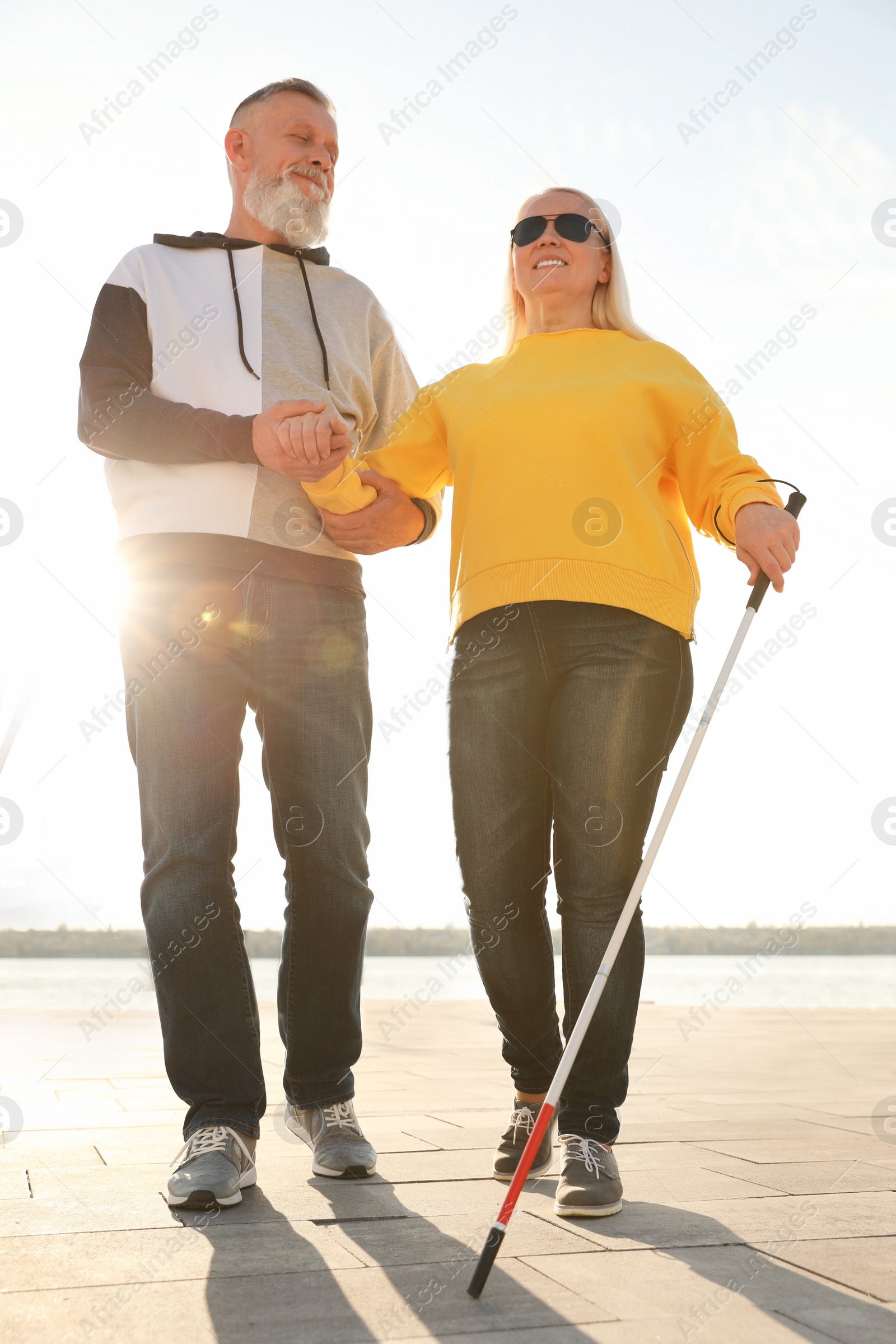 Photo of Mature man helping blind person with long cane outdoors