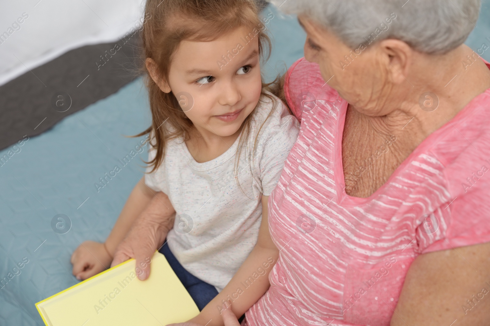 Photo of Cute girl and her grandmother reading book on bed at home