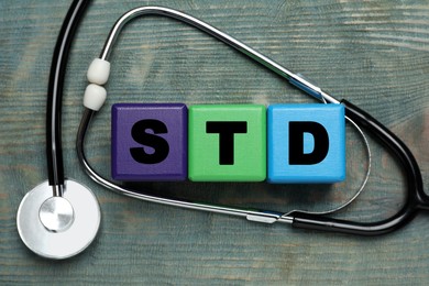 Abbreviation STD made with cubes near stethoscope on light blue wooden table, flat lay