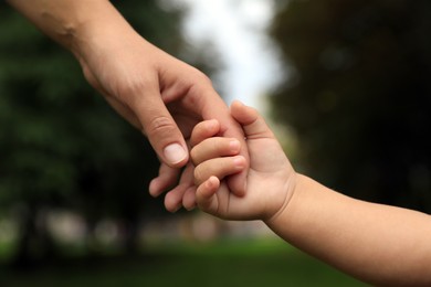Photo of Daughter holding mother's hand in park, closeup. Happy family