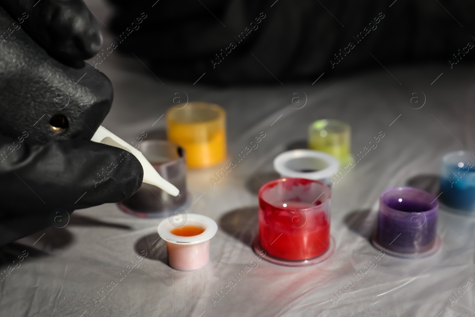 Photo of Tattoo artist dipping machine needle into ink at table, closeup