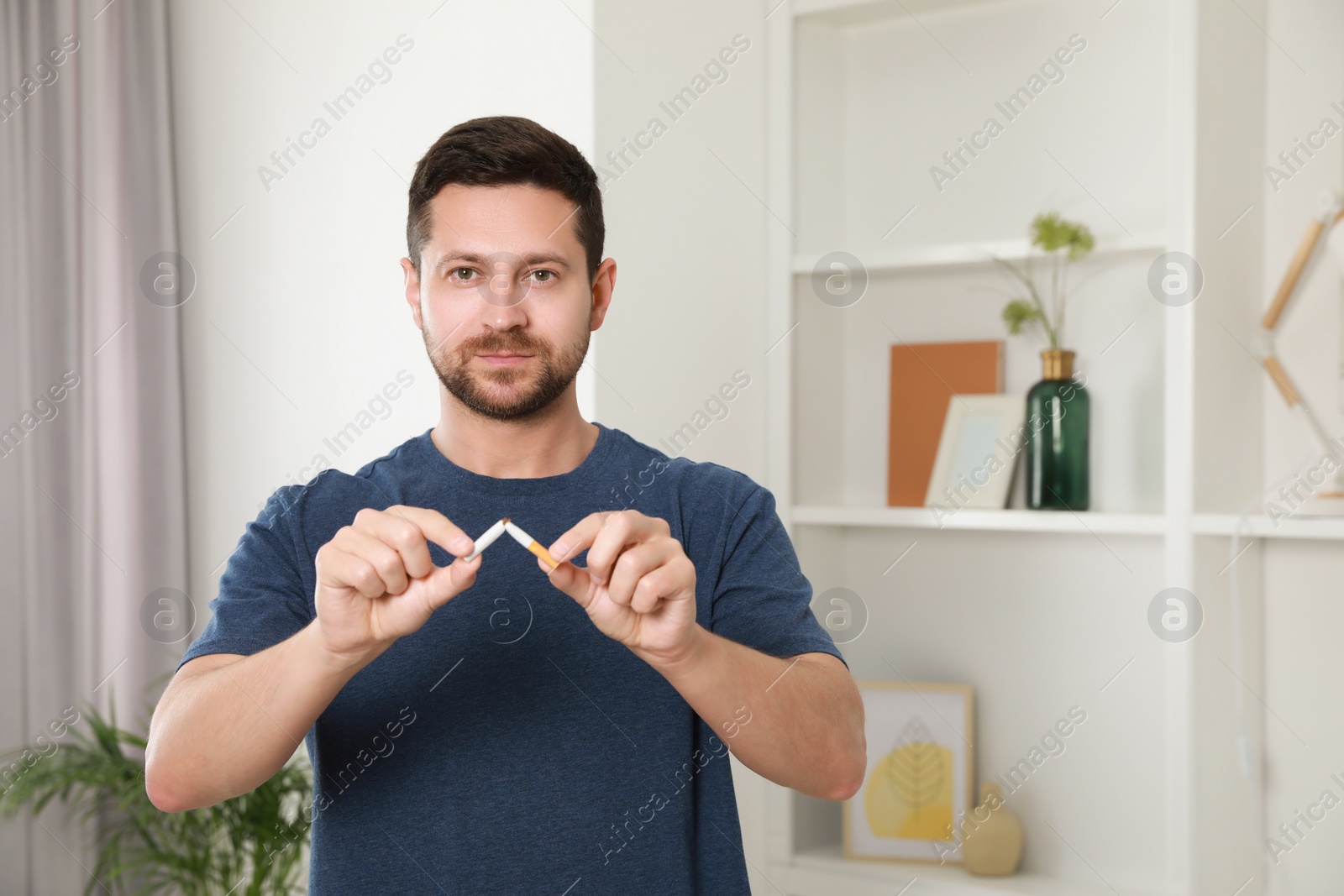 Photo of Stop smoking concept. Man holding pieces of broken cigarette at home, space for text