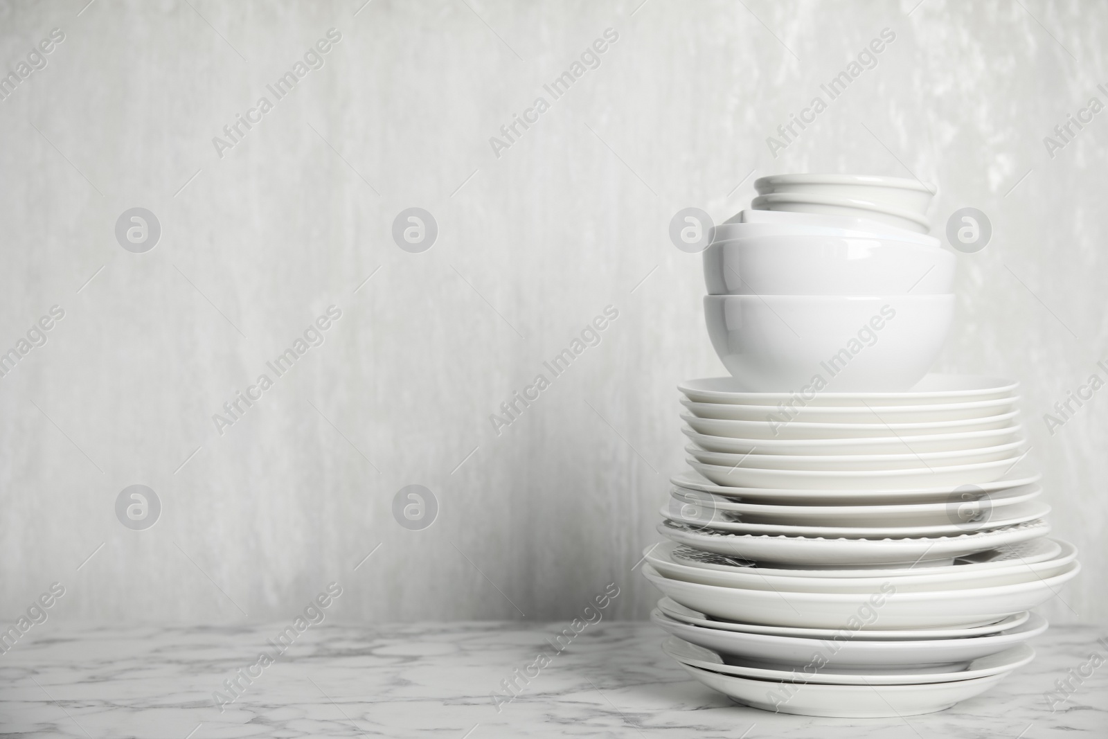 Photo of Stack of clean tableware on white marble table. Space for text
