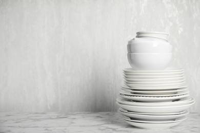 Photo of Stack of clean tableware on white marble table. Space for text