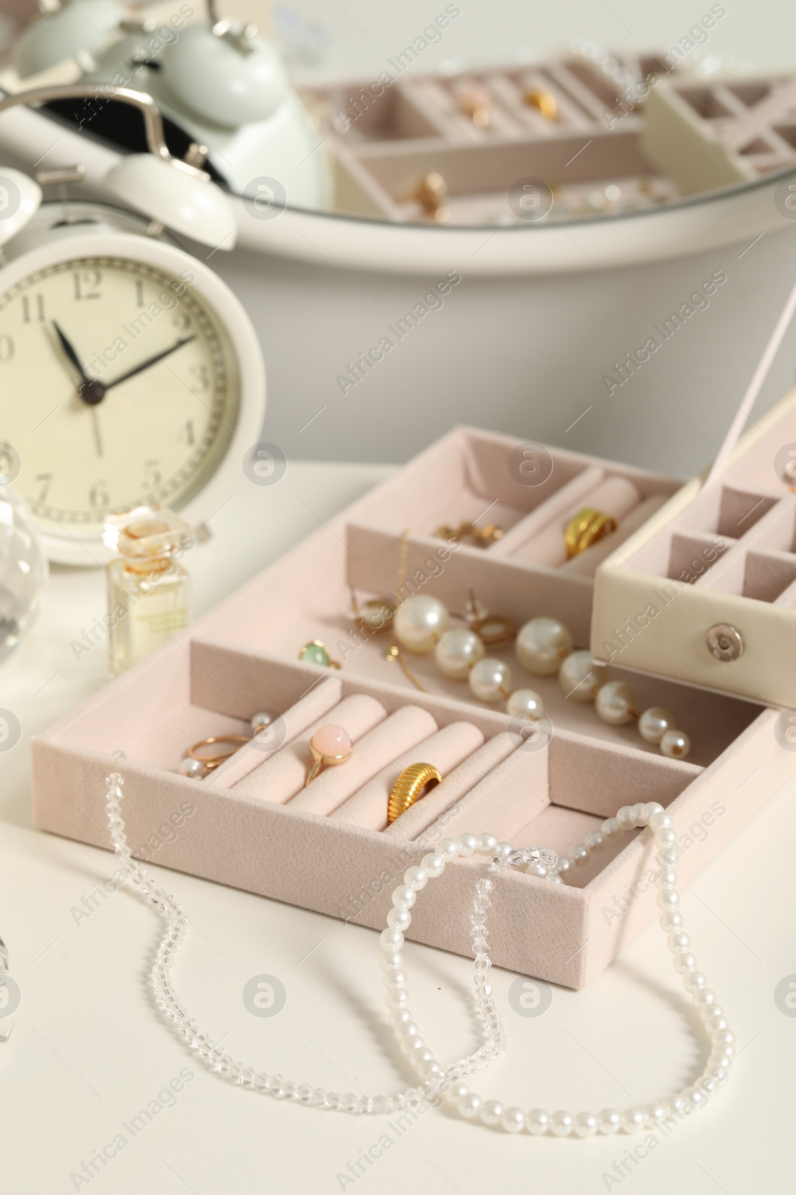 Photo of Jewelry boxes with many different accessories, perfume and alarm clock on white table